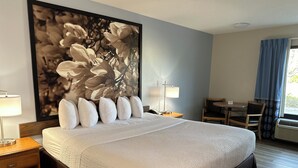 Habitación de hotel con una cama grande, un escritorio, una silla y una obra de arte floral enmarcada en la pared.