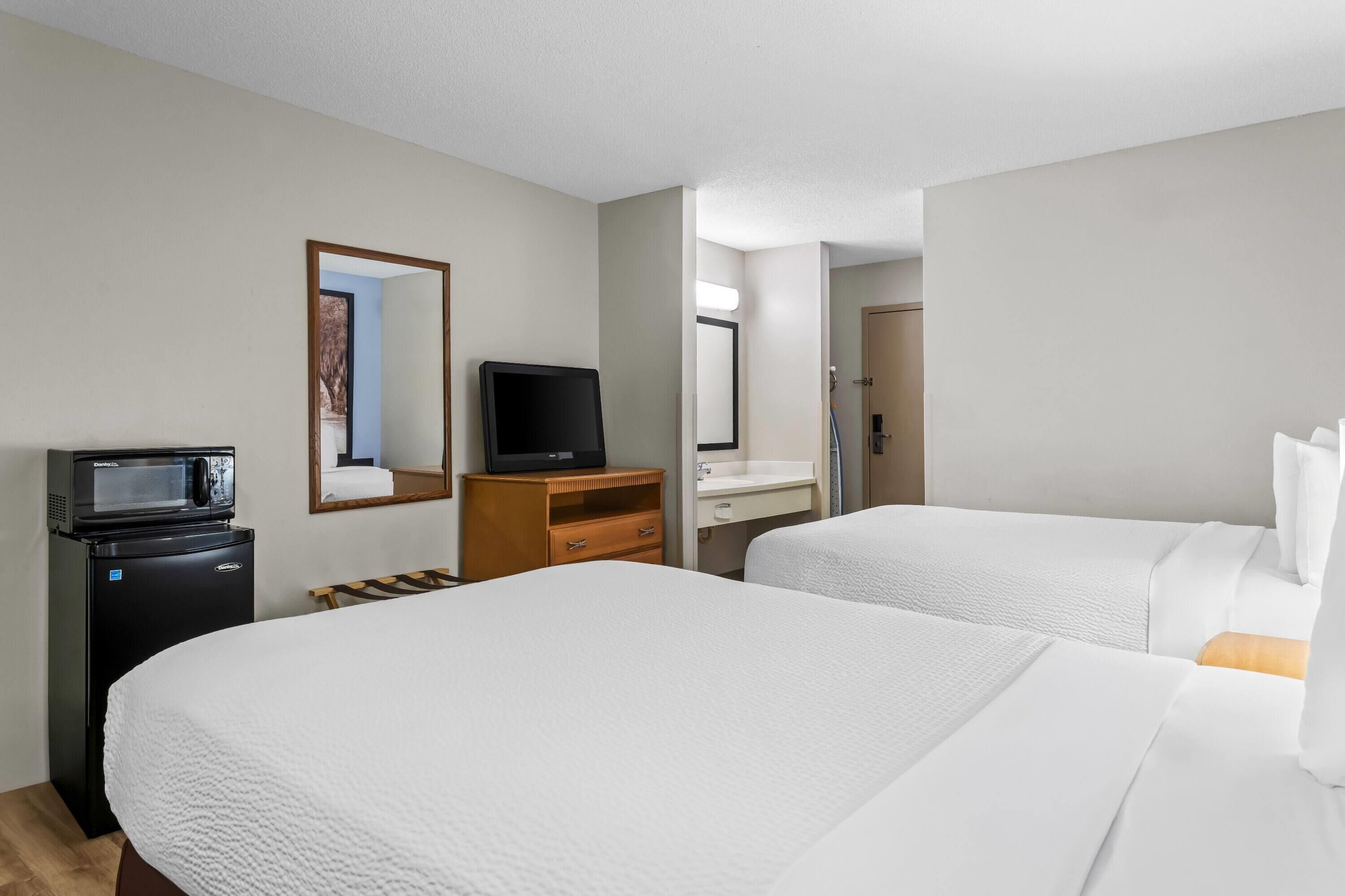 A hotel room with two beds, a microwave, a television, a wooden dresser, and a bathroom visible through an open door.