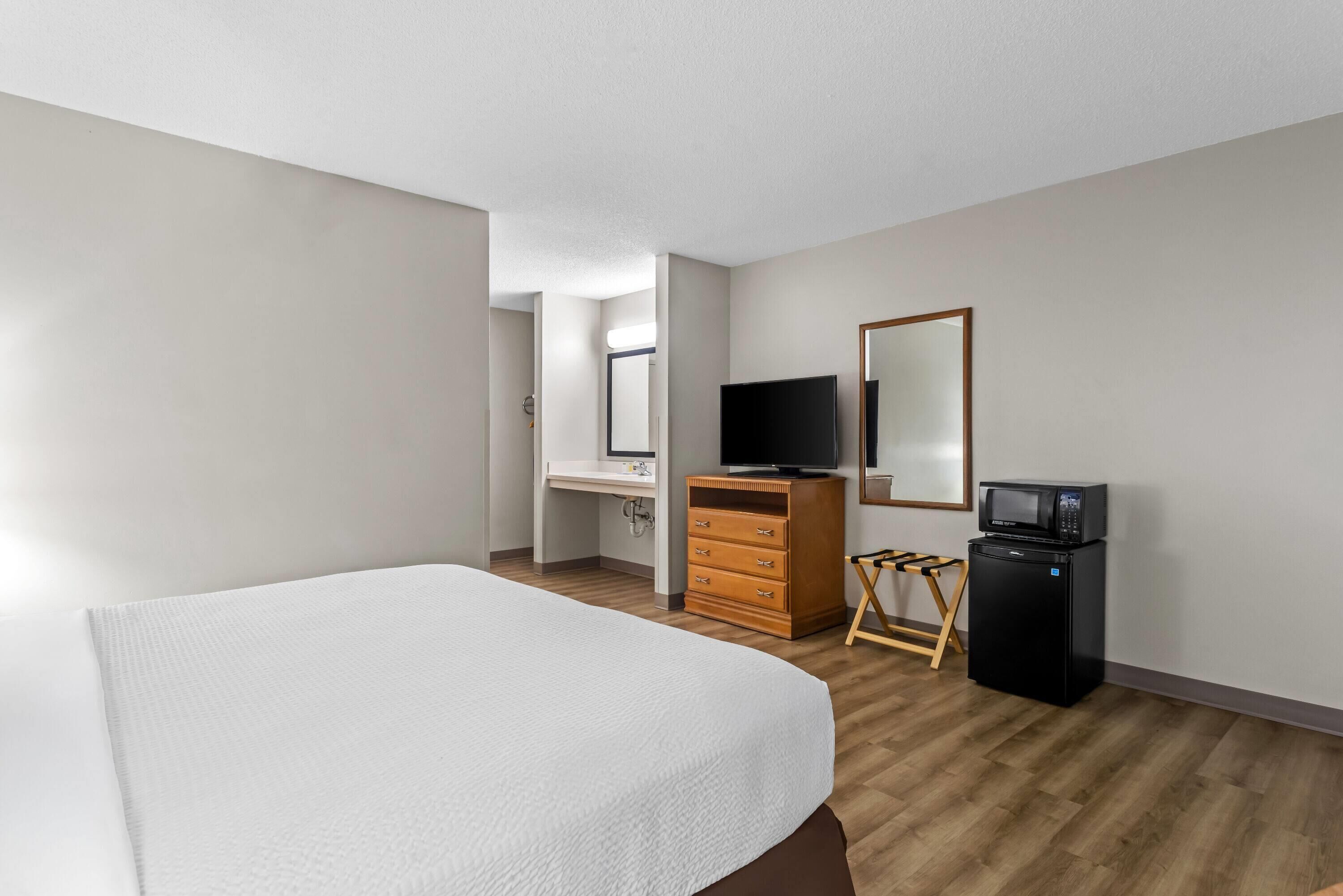 A hotel room with a bed, a dresser, a television, a microwave, and a mirror.