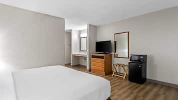 Quarto de hotel com cama, penteadeira, televisão, micro-ondas e espelho.