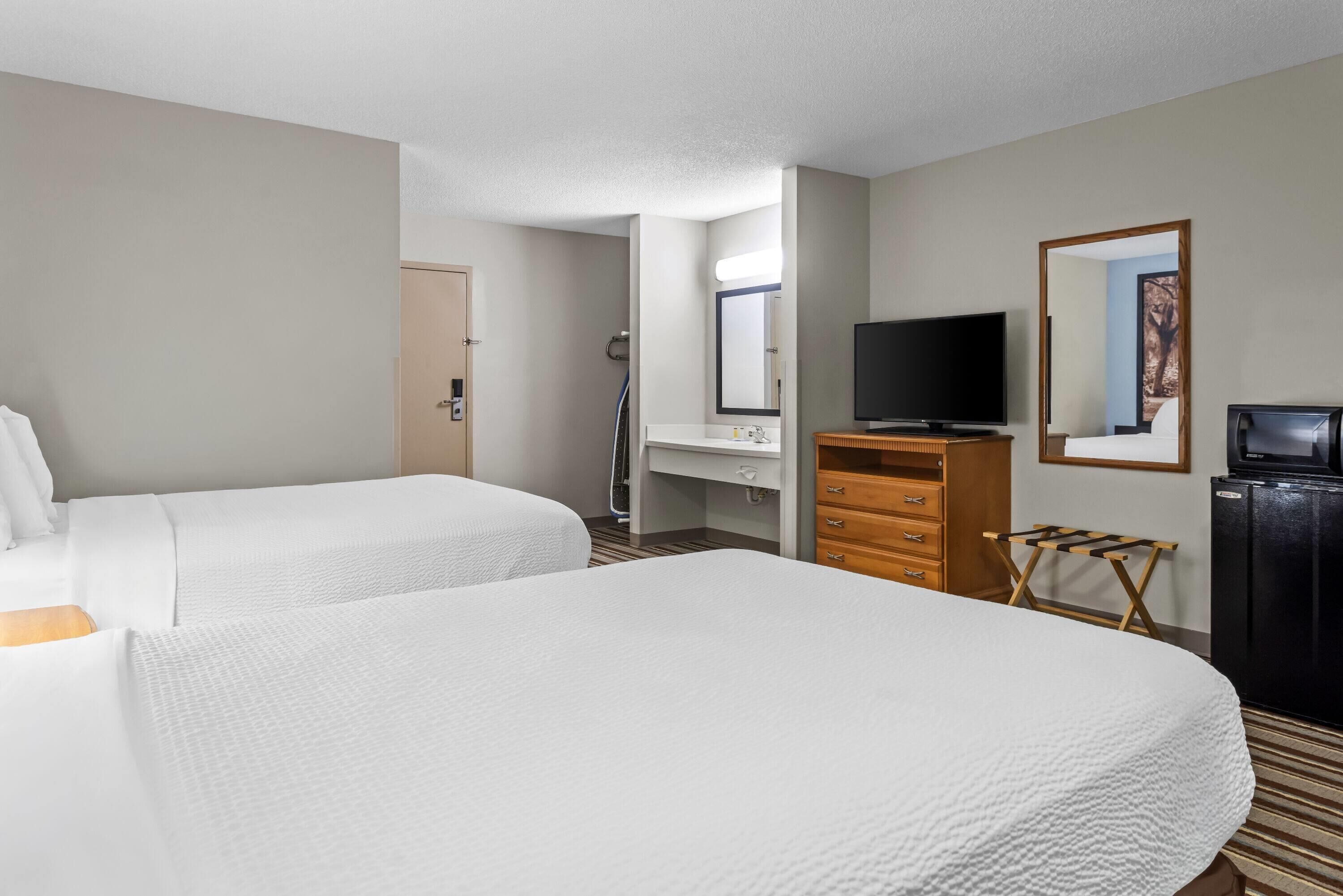 A hotel room with two beds, a desk with a mirror, a television, and a wardrobe.