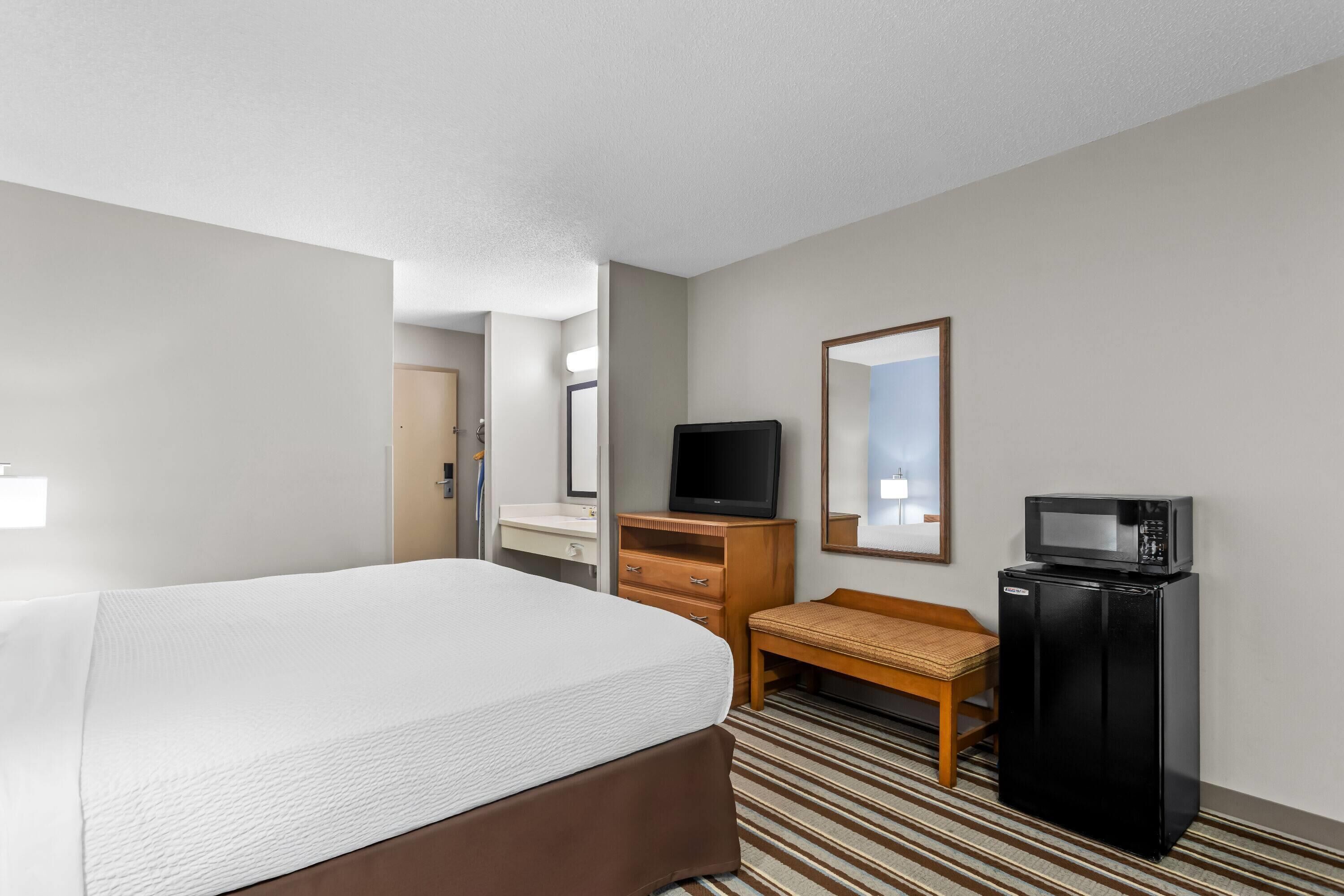 A hotel room with a bed, a television, a microwave, a desk, and a mirror.