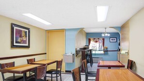 Un restaurante con mesas y sillas de madera, un cuadro en la pared y una puerta que da a otra habitación.