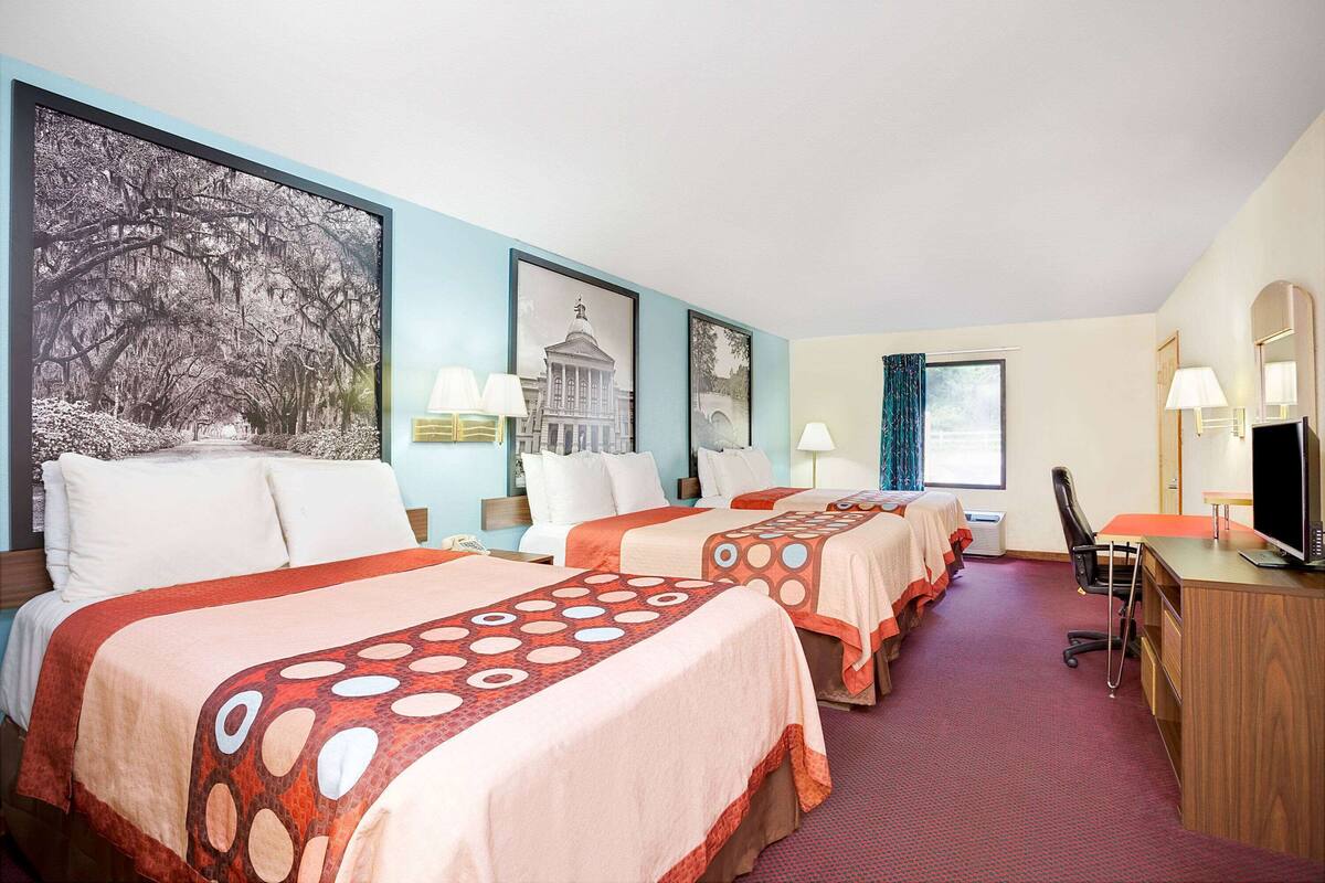 Camera d'albergo con tre letti, una scrivania con un computer e una televisione.