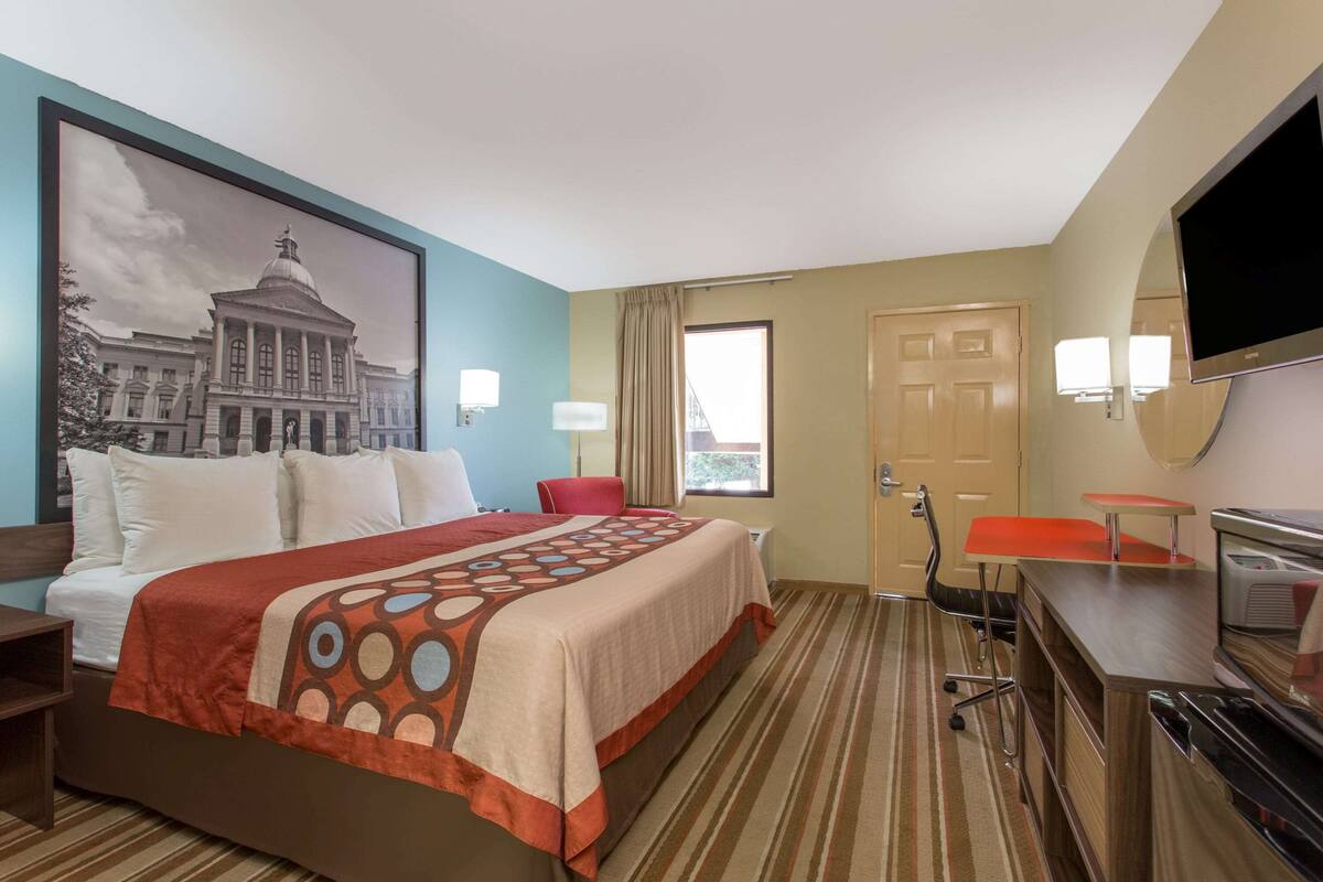 Una camera d'albergo con un letto grande, una scrivania, una sedia, una televisione e una finestra con tende.