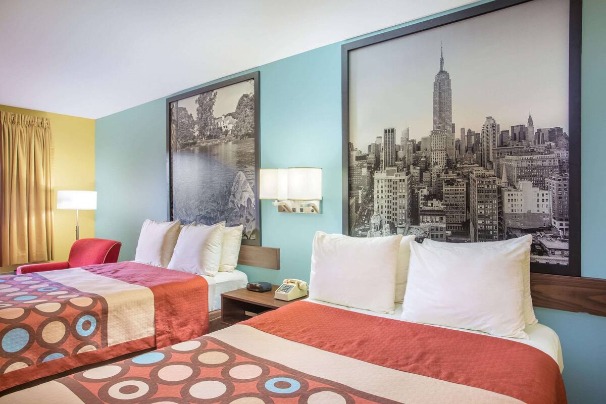Camera d'albergo con due letti, un quadro raffigurante un panorama urbano, una lampada e un telefono sul comodino.