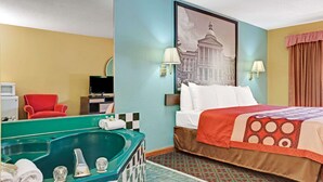 Habitación de hotel con una cama grande, una bañera verde, un sillón rojo y un cuadro de un edificio en la pared.