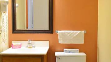 A bathroom with an orange wall, a wooden vanity with a mirror above it, a white toilet, and a towel hanging on a rack.