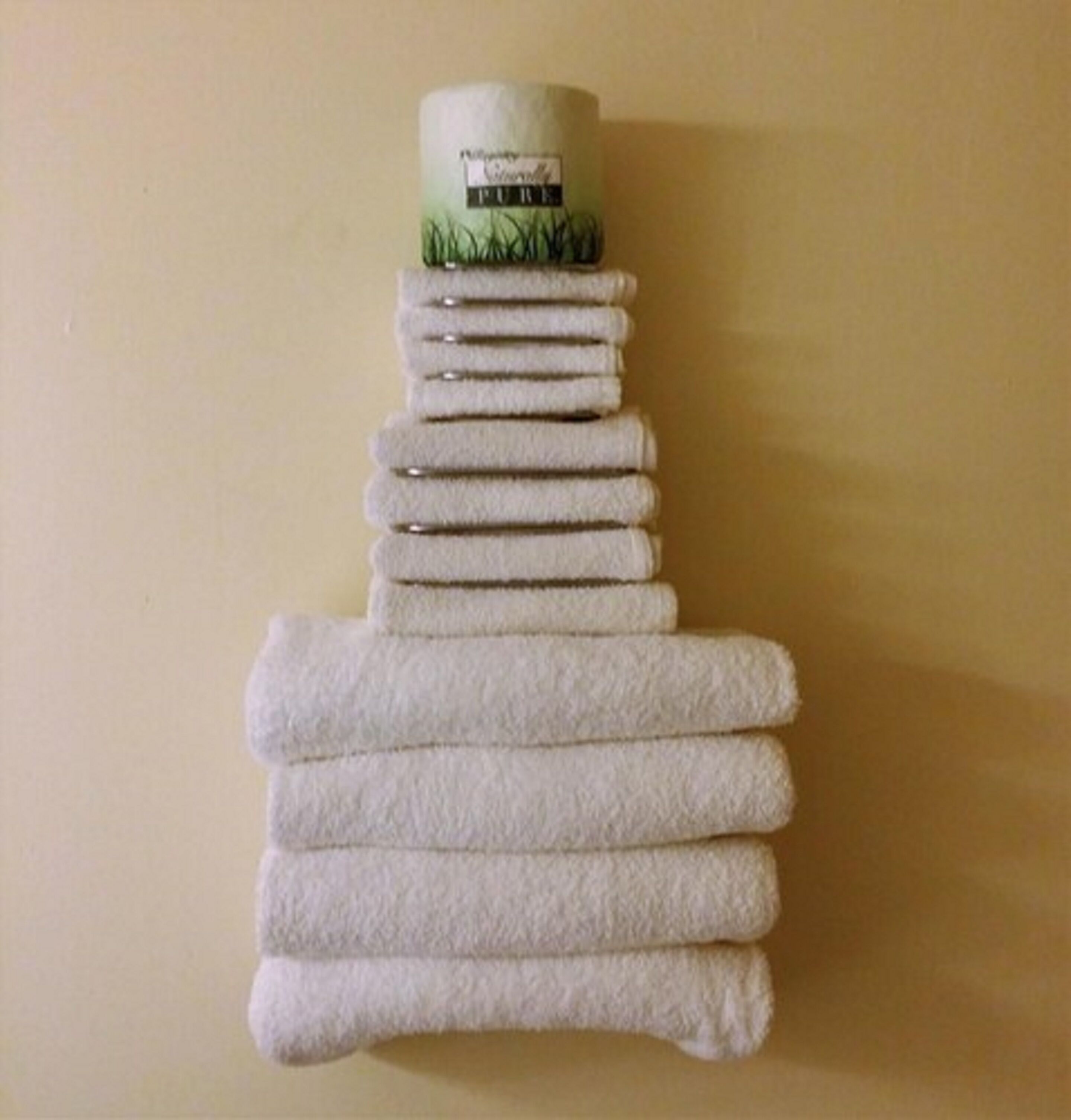 A stack of white towels arranged in a pyramid shape on a plain wall.