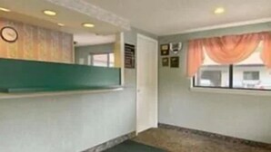 A reception area with a counter, a clock, and a window with curtains. - Enfield Inn (Enfield)