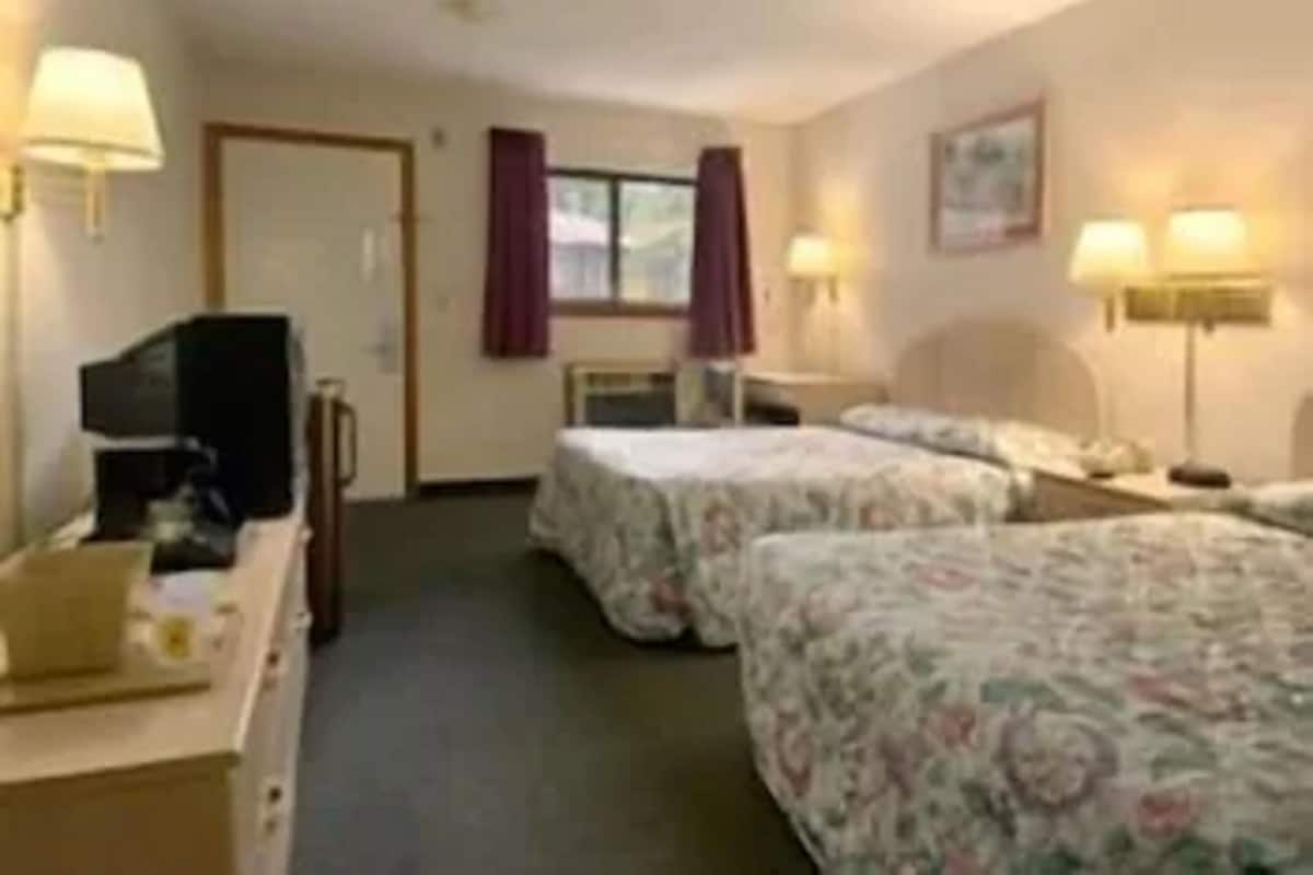 A hotel room with two beds, a desk, a television, and a window with curtains.