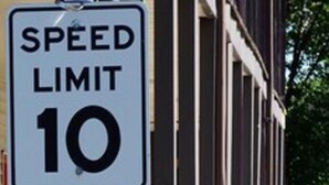 A speed limit sign of 10 mph on a street with a building and flower pots. - Enfield Inn (Enfield)