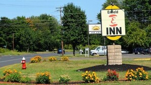 A sign for Enfield Inn with a yellow and black logo, surrounded by a landscaped area with flowers and a fire hydrant. - Enfield Inn (Enfield)