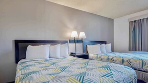 A hotel room with two beds, each with a patterned bedspread, a nightstand with a lamp, and a window with curtains.