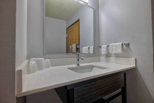 Un baño con un lavabo blanco, un espejo y dos toallas colgadas en un perchero.