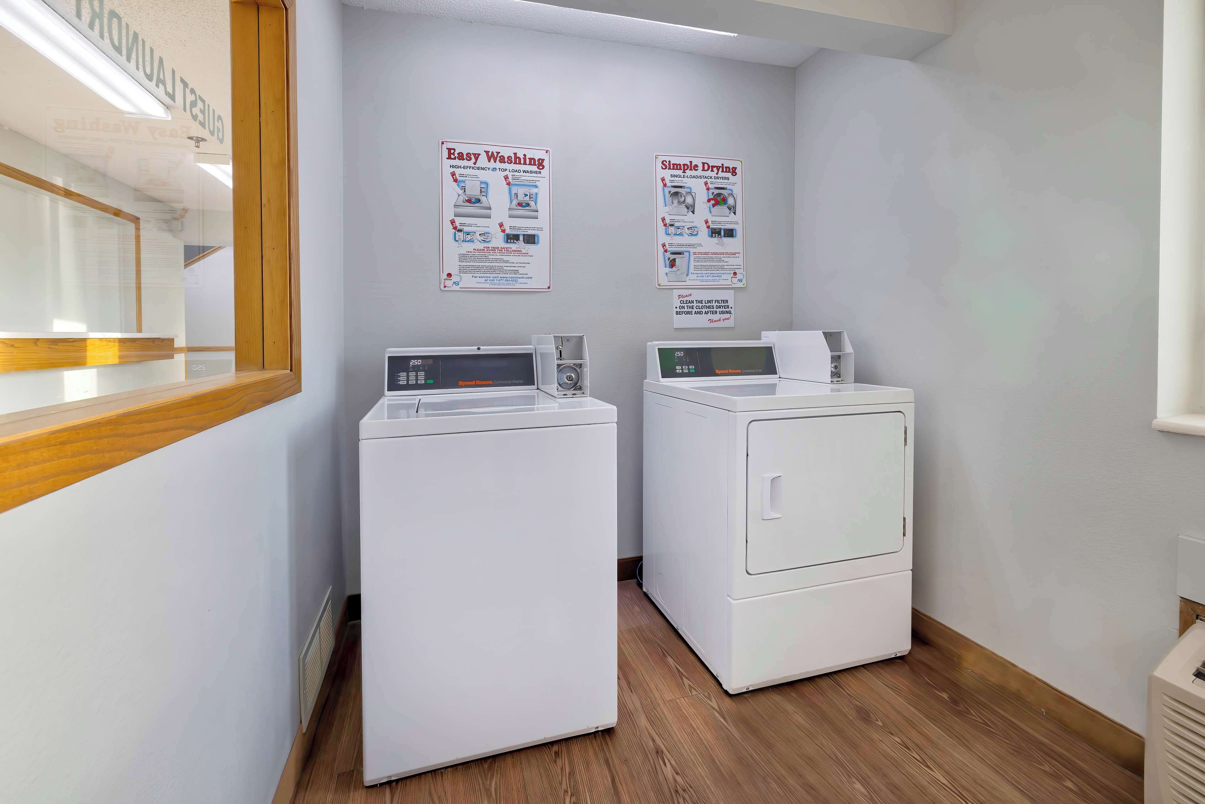 A laundry area with two washing machines and dryers, wooden flooring, and instructional posters on the wall.