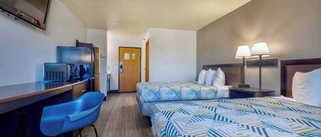 Habitación de hotel con escritorio, dos camas, una silla, televisor y lámpara.