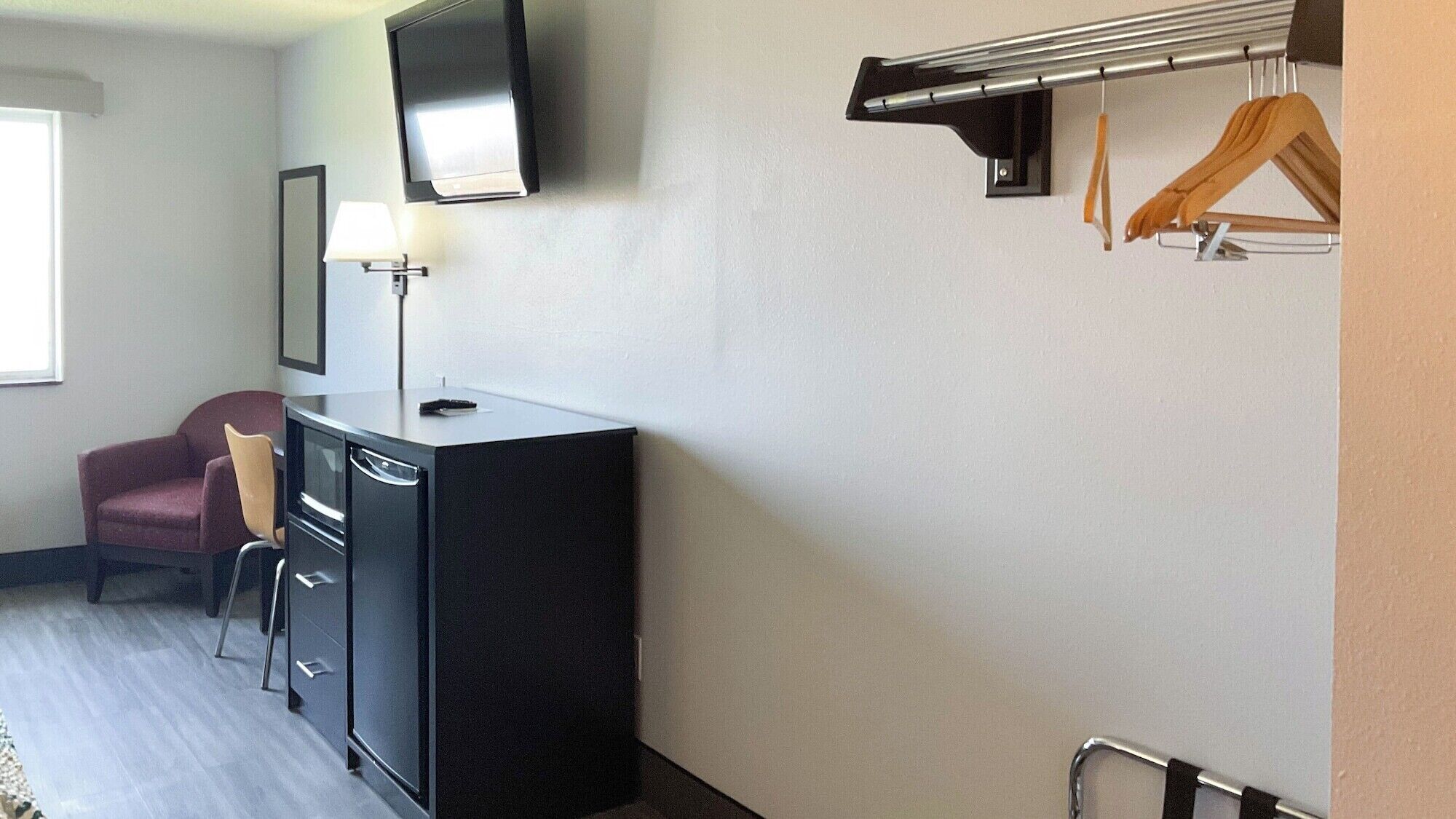 A compact room with a desk, chair, TV, and a coat rack with hangers.