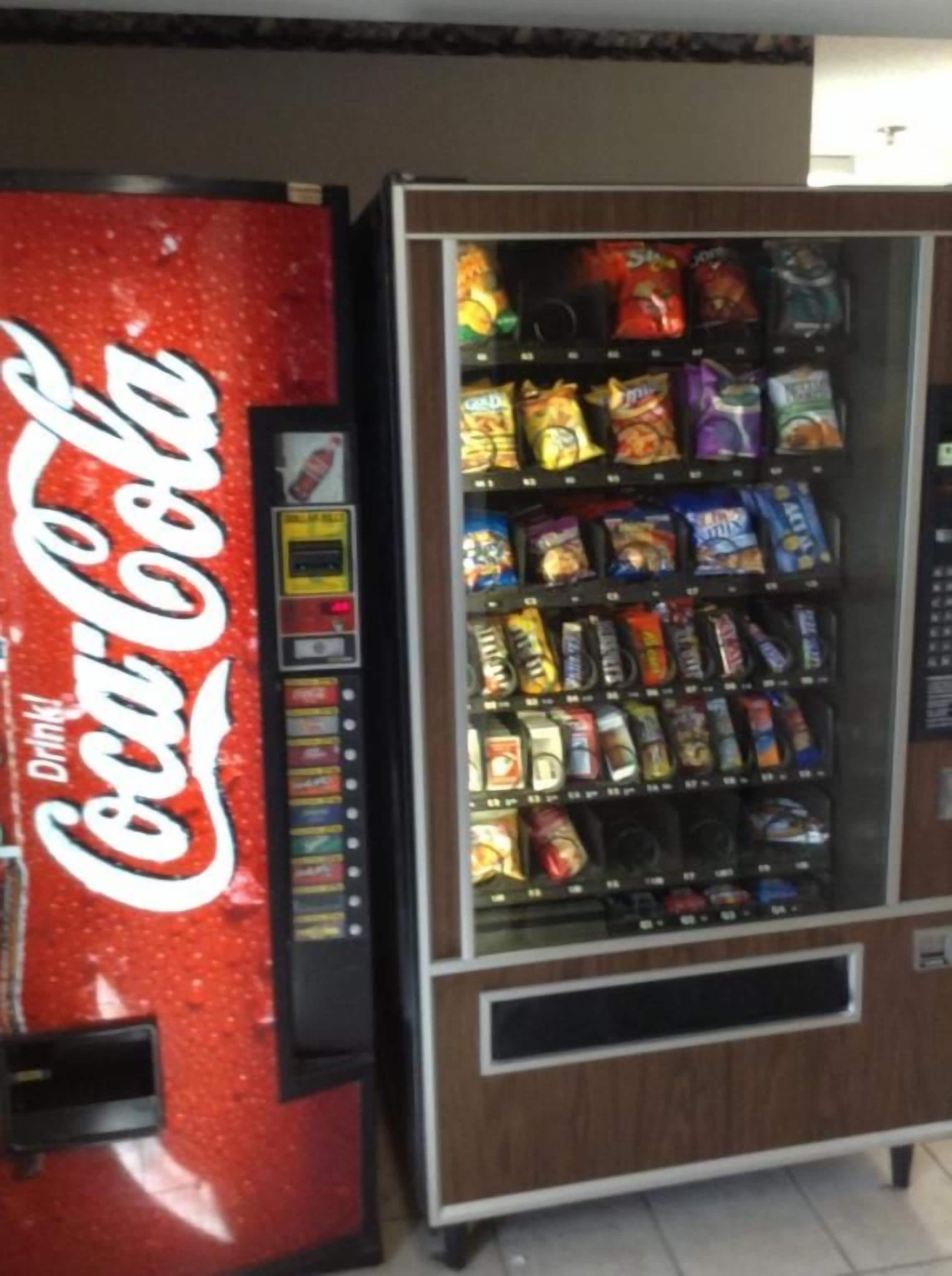 Máquina expendedora con logotipo de Coca-Cola y otra máquina expendedora de productos de snack envasados.