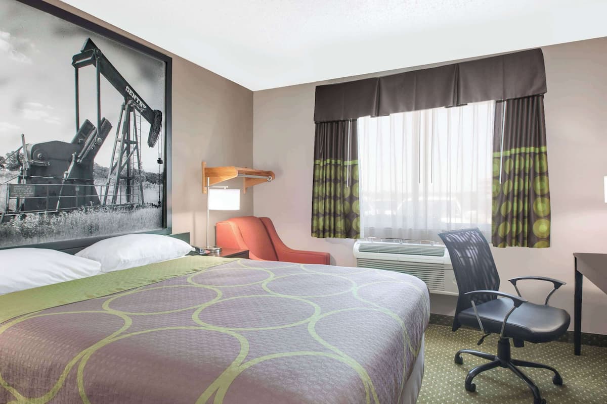 Ein Hotelzimmer mit einem großen Bett, einem Schreibtisch, einem Stuhl, einem fenster mit Vorhängen und einer Wand-Klimaanlage.