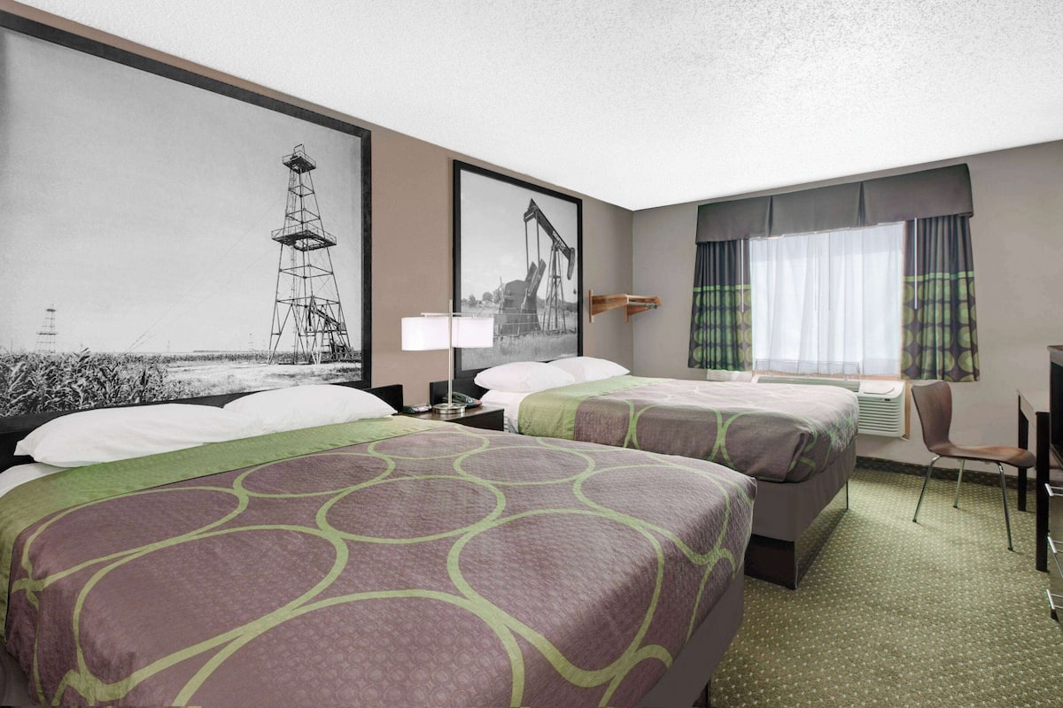 Ein Hotelzimmer mit zwei Betten, einem Schreibtisch, einem Stuhl und großen Fenstern mit Vorhängen.