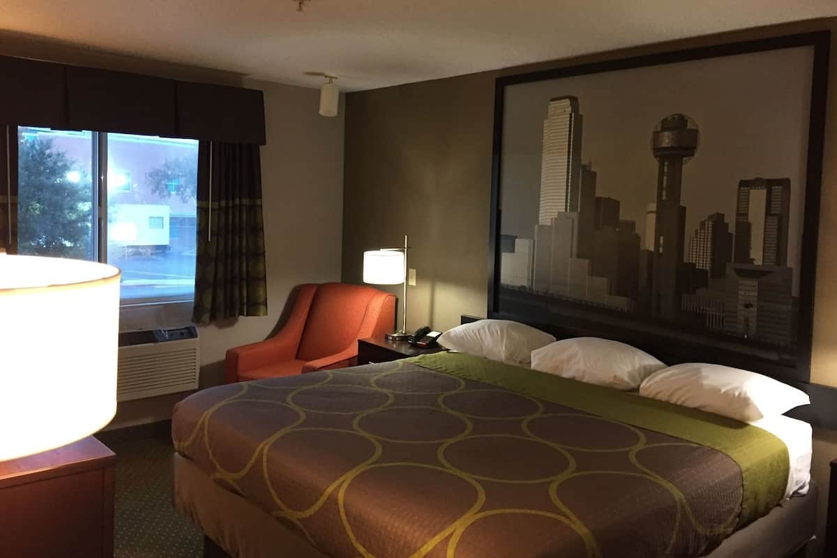 Ein Hotelzimmer mit Bett, Sessel, Schreibtisch mit Lampe, Fenster mit Blick und einem Stadtbild an der Wand.