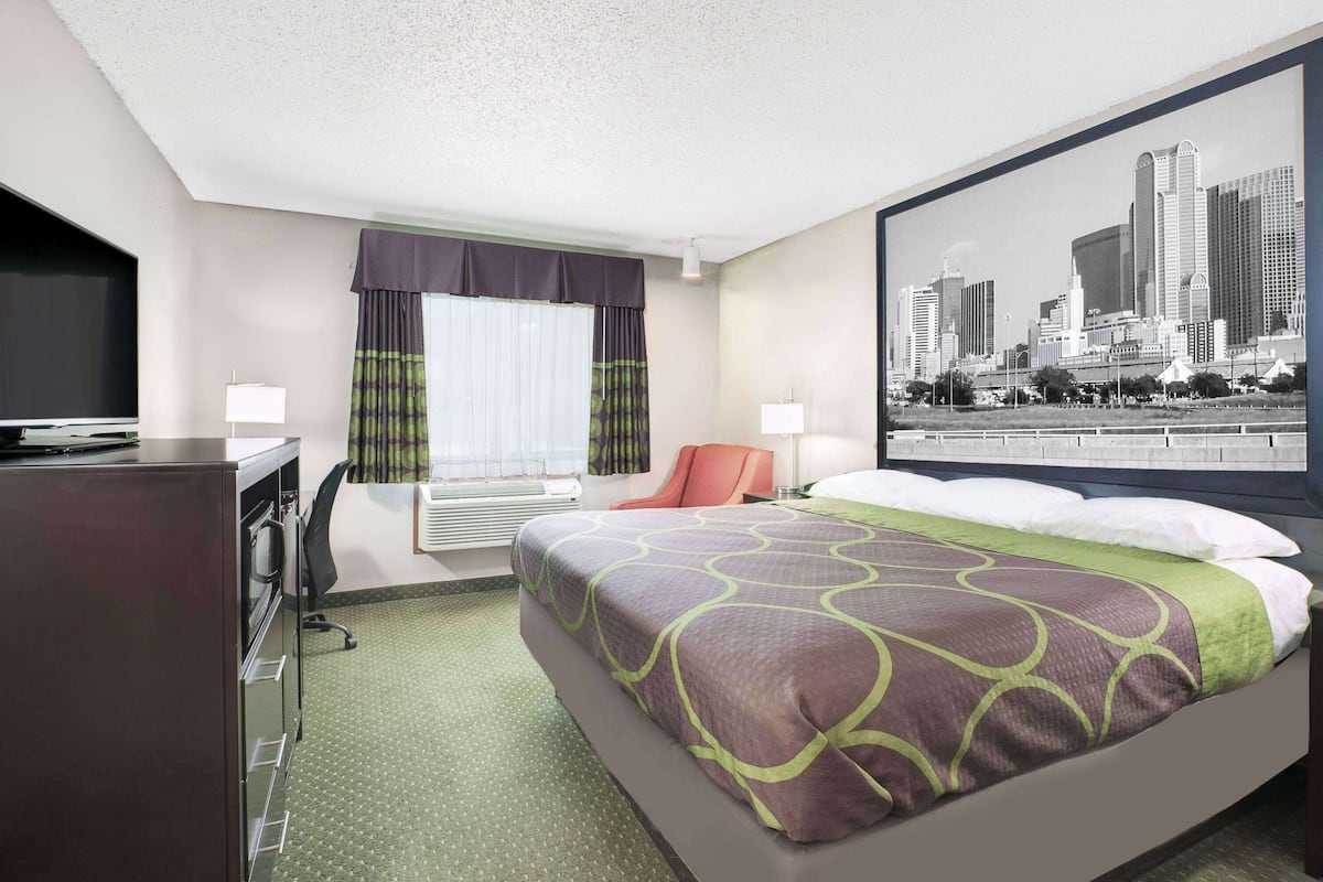 Ein Hotelzimmer mit Bett, Schreibtisch mit Fernseher, Fenster mit Vorhängen und einem Stadtlandschaftsposter an der Wand.