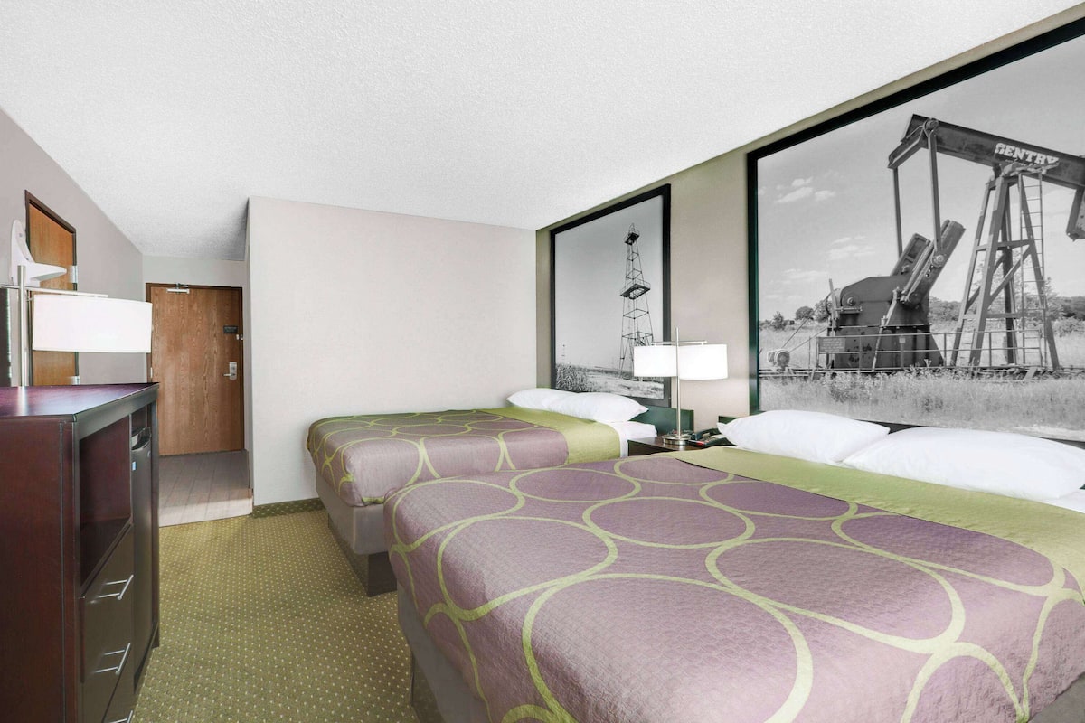 Ein Hotelzimmer mit zwei Betten, einem Schreibtisch und einem großen gerahmten Bild einer Ölplattform.