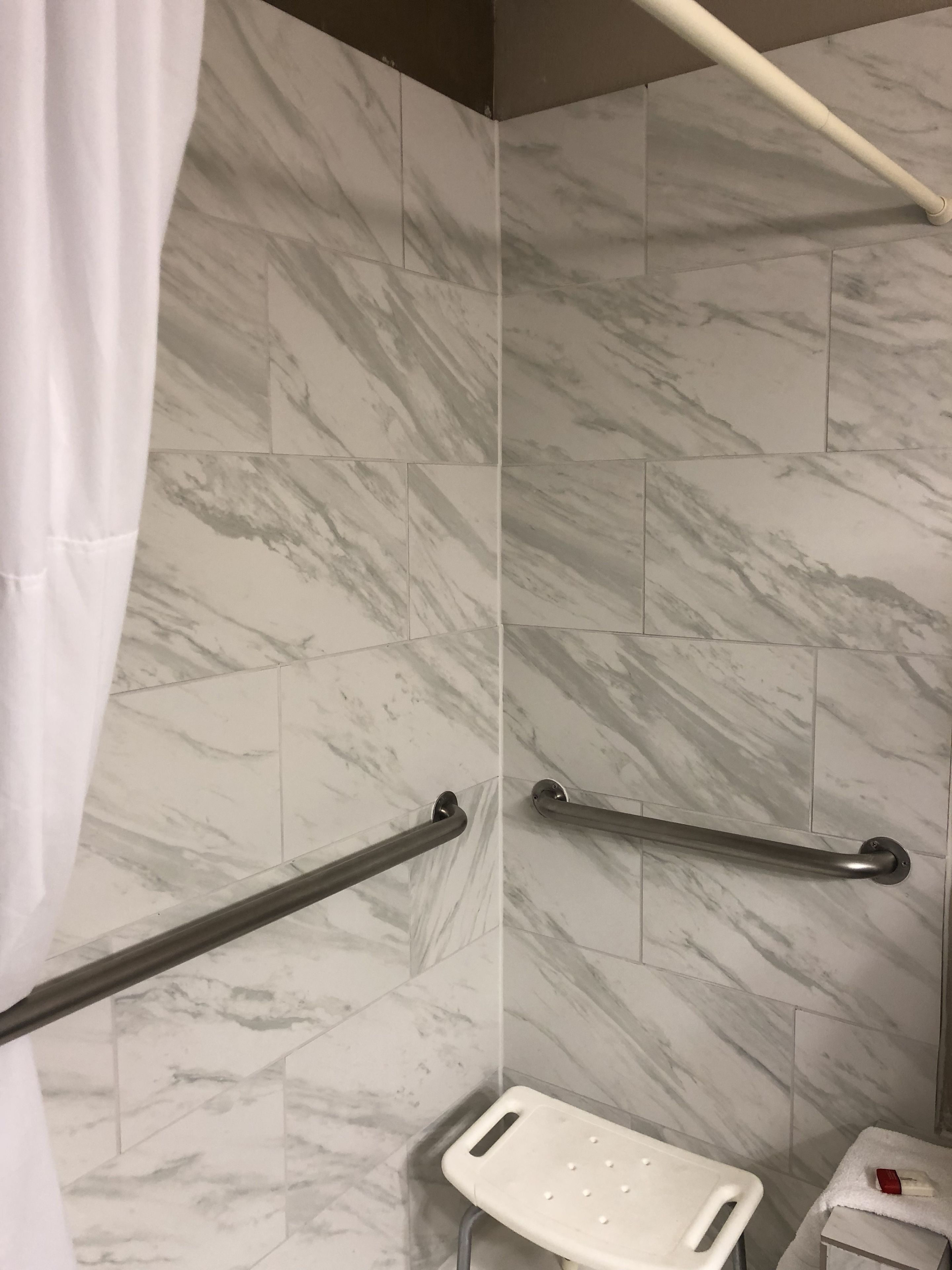 Ein Badezimmer mit Marmorwänden, einer Dusche inklusive Haltegriff, einem weißen Duschhocker und einem Handtuch auf einem kleinen Tisch.