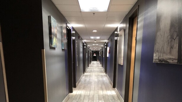 A long, narrow hallway with a wooden floor, dark walls, and doors on both sides.