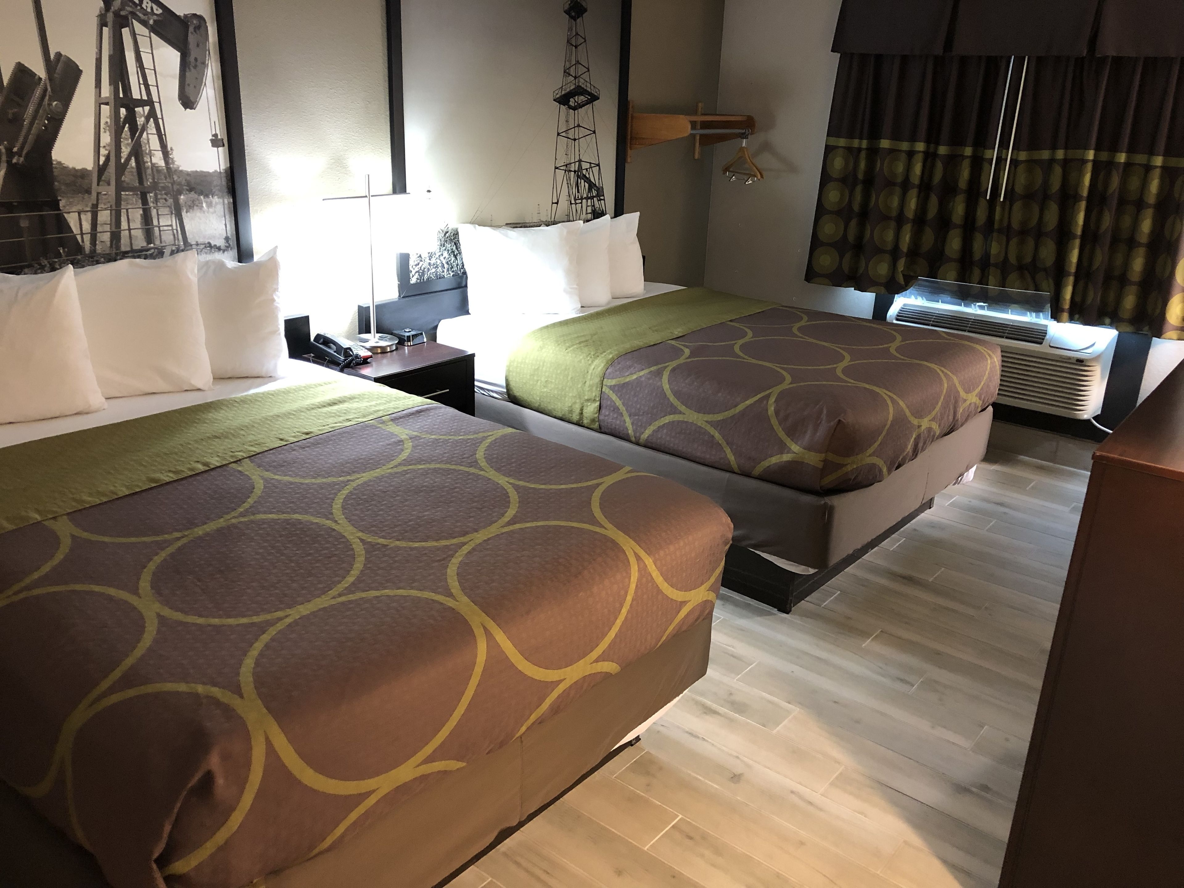 Una habitación de hotel con dos camas, una mesita de noche, una lámpara, un teléfono, una ventana con cortinas y un equipo de aire acondicionado.