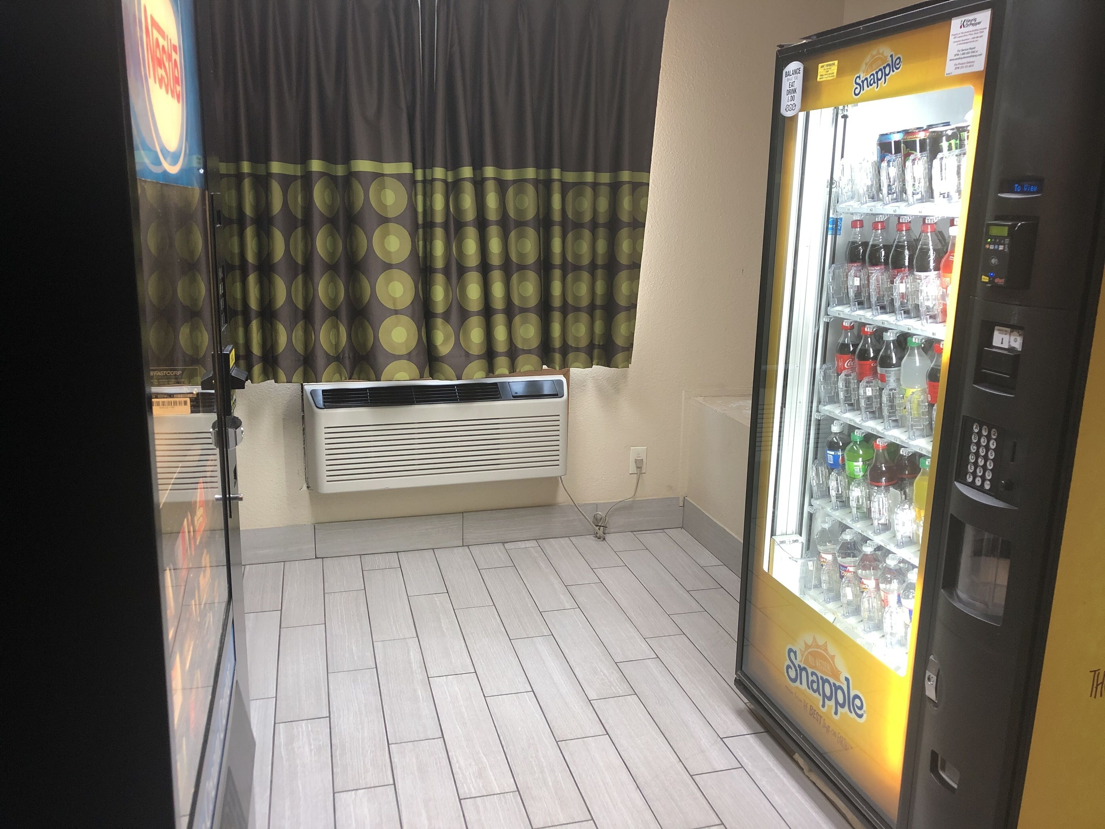 A Snapple vending machine and a wall-mounted air conditioner in a room with tiled flooring.