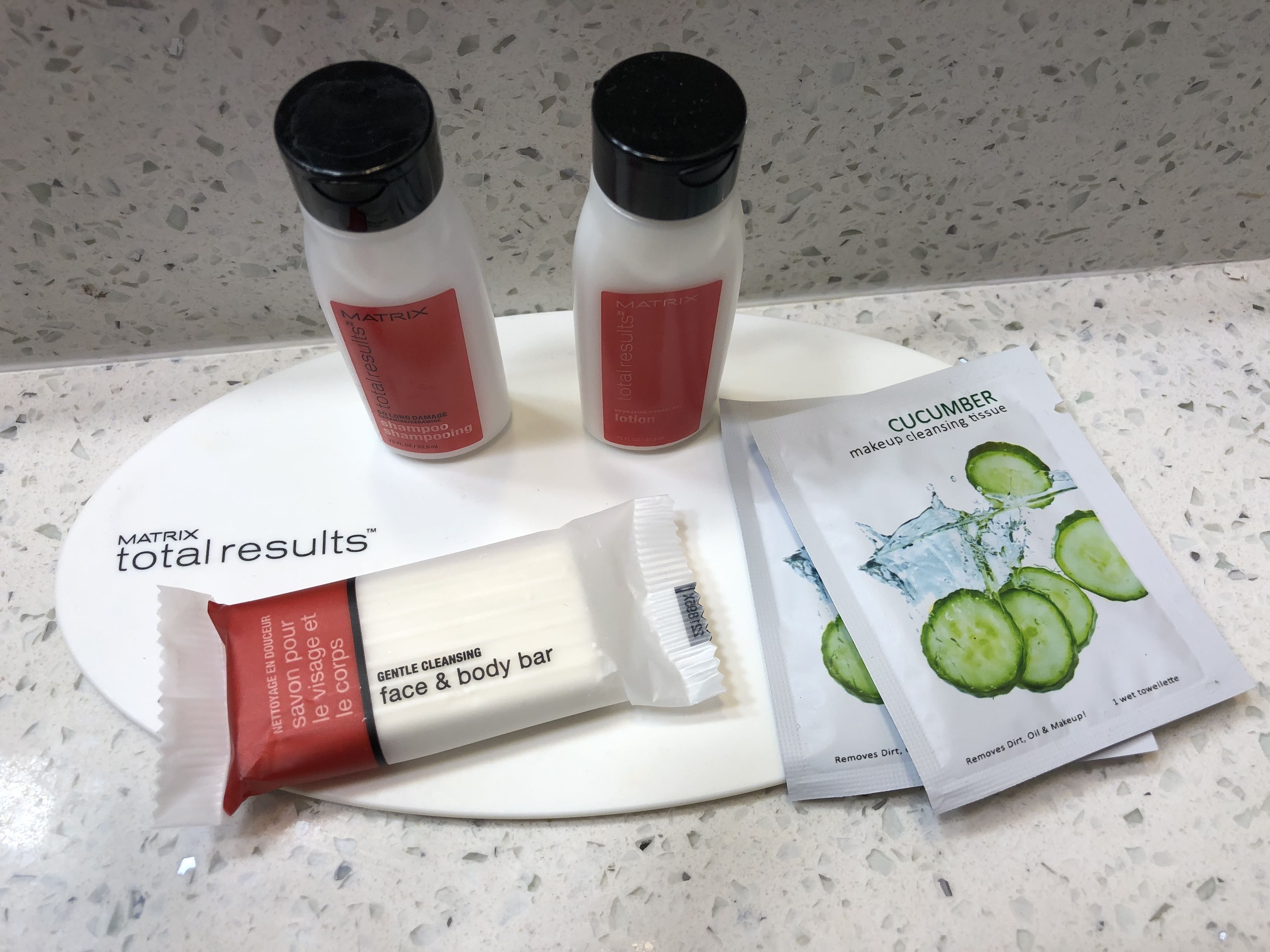 A countertop with a white plate displaying various skincare products including a face and body bar, a cucumber cleansing wipe, and two bottles of Matrix Total Results shampoo.