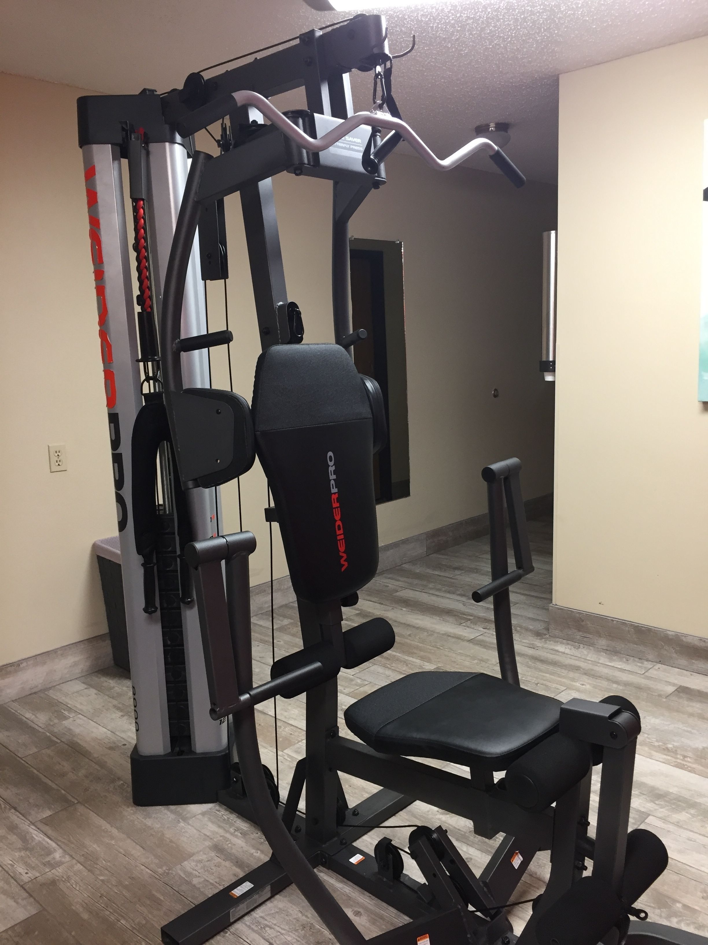 A gym with a multi-functional workout machine, a bench, and a wall-mounted mirror.