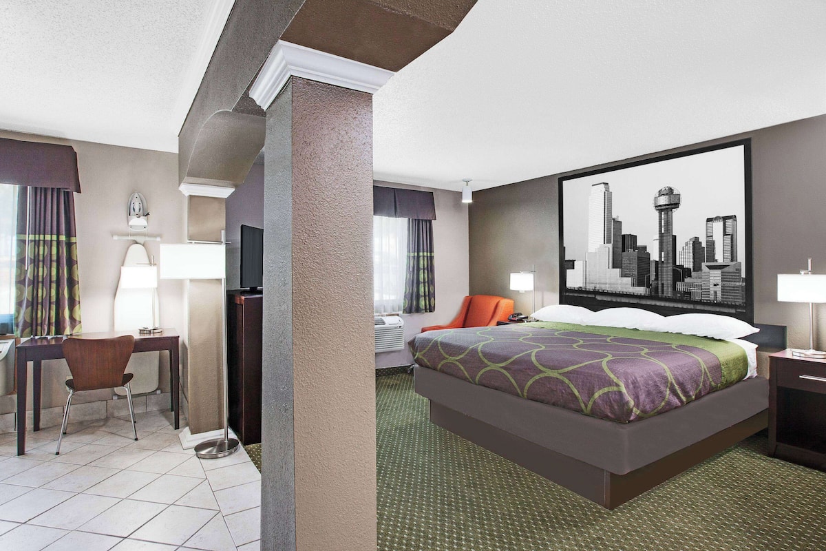 Ein Hotelzimmer mit Bett, Schreibtisch, Stuhl, Fernseher und einem Stadtbild an der Wand.