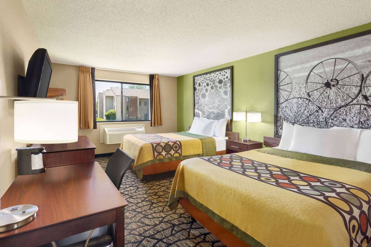 A hotel room with two beds, a desk, a chair, a TV, and a window with curtains.