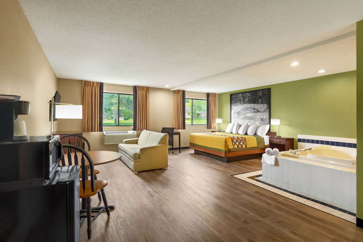 A hotel room with a bed, a desk, a chair, a sofa, a bathtub, and a window with curtains.