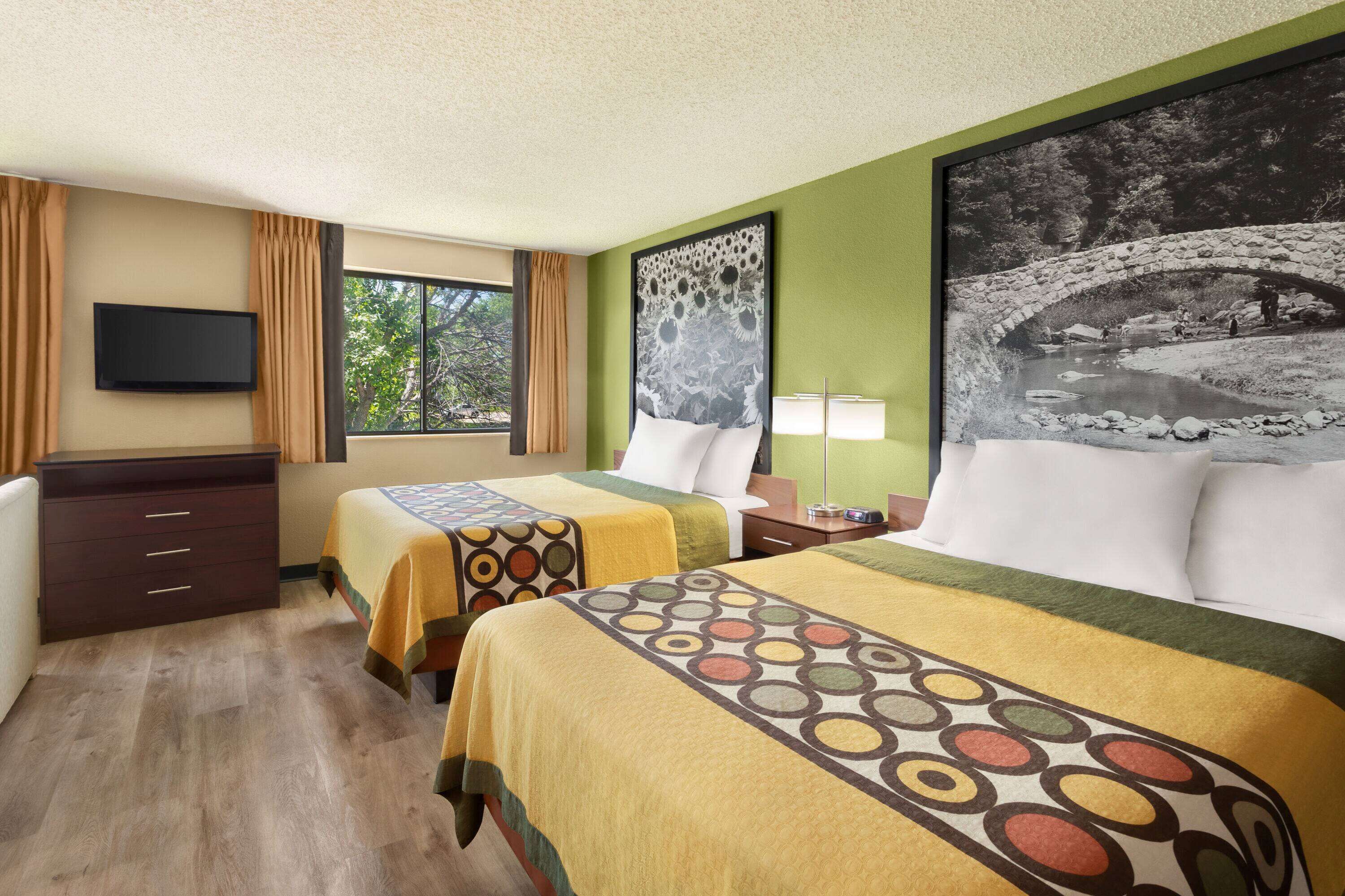 A hotel room with two beds, a TV, a desk, and a window with curtains.
