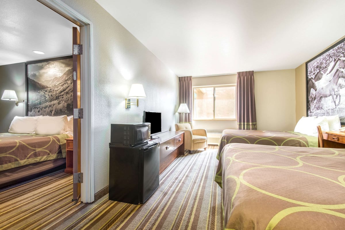A hotel room with two beds, a desk, a television, and a window with curtains.