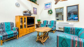A living room with patterned sofas, a wooden cabinet, a coffee table, a television, and a mounted animal hide. - Super 8 by Wyndham Buena Vista (Buena Vista)