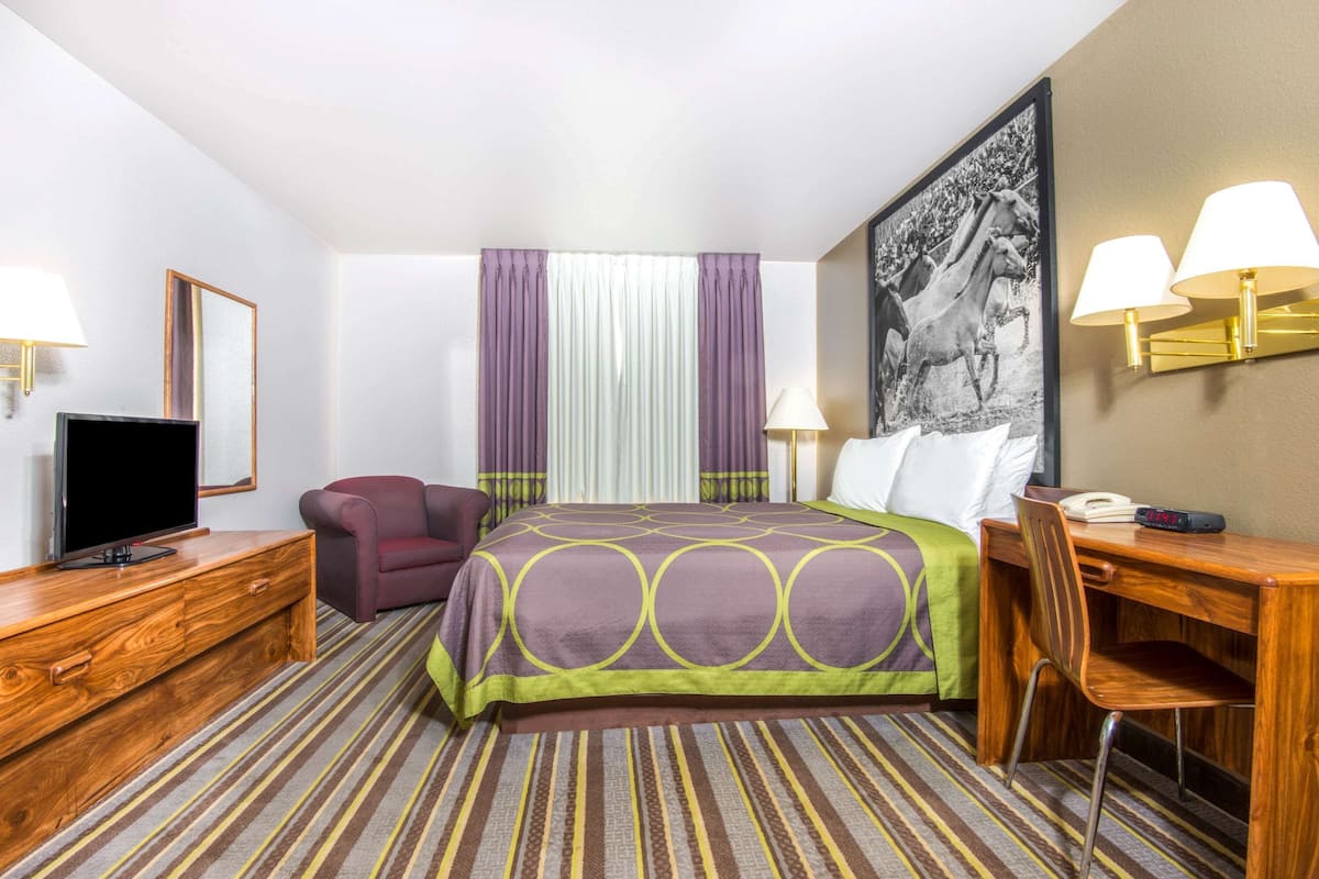 A hotel room with a bed, a desk, a chair, a television, and a painting on the wall.