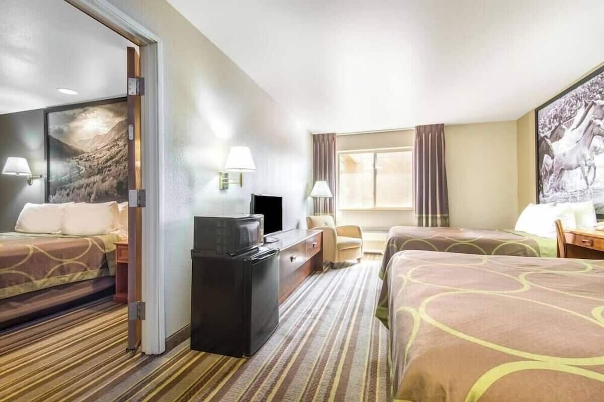 A hotel room with two beds, a desk, a TV, and a painting on the wall.