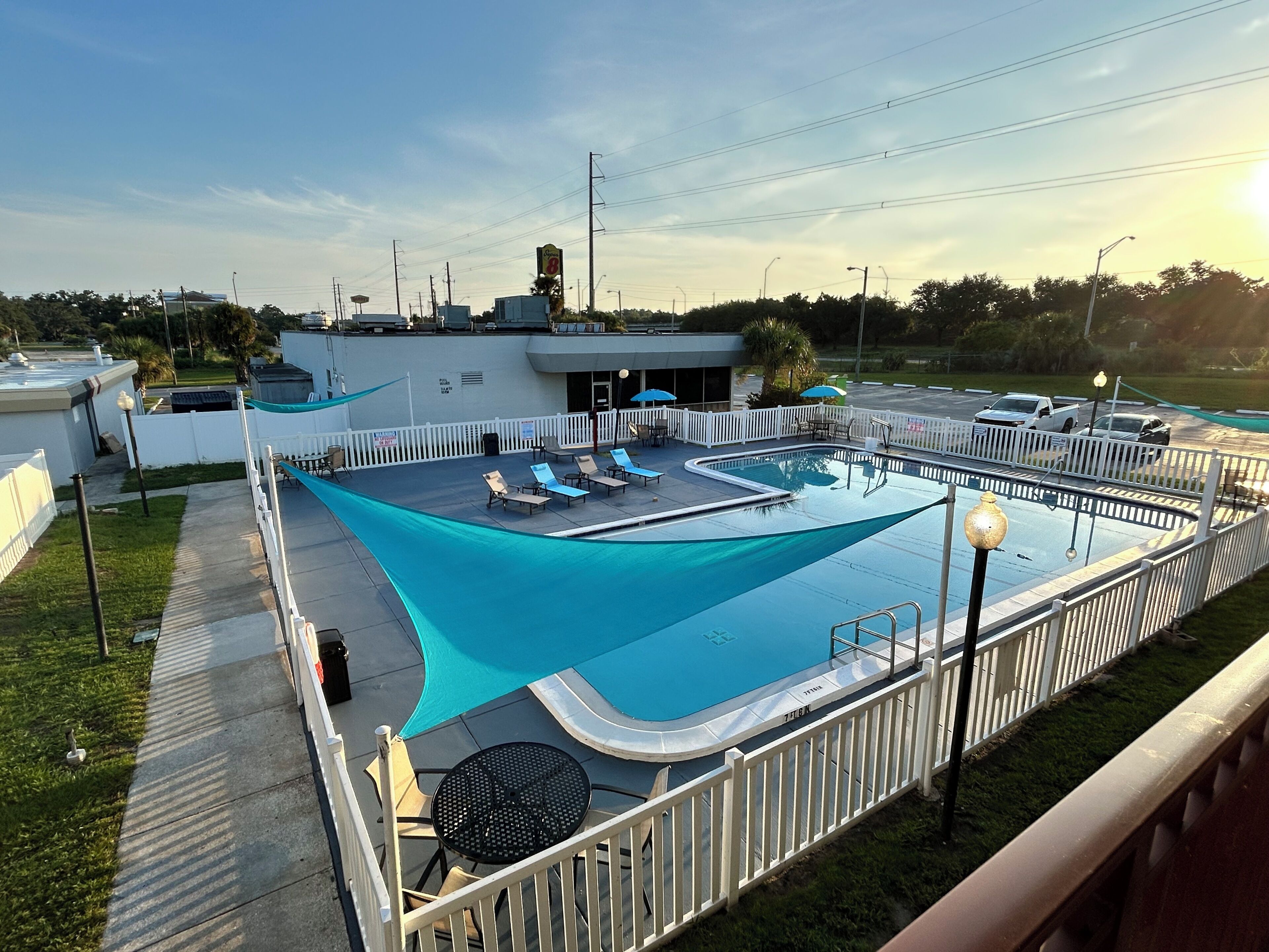 A rooftop pool with sun loungers and a covered seating area, surrounded by a white fence.