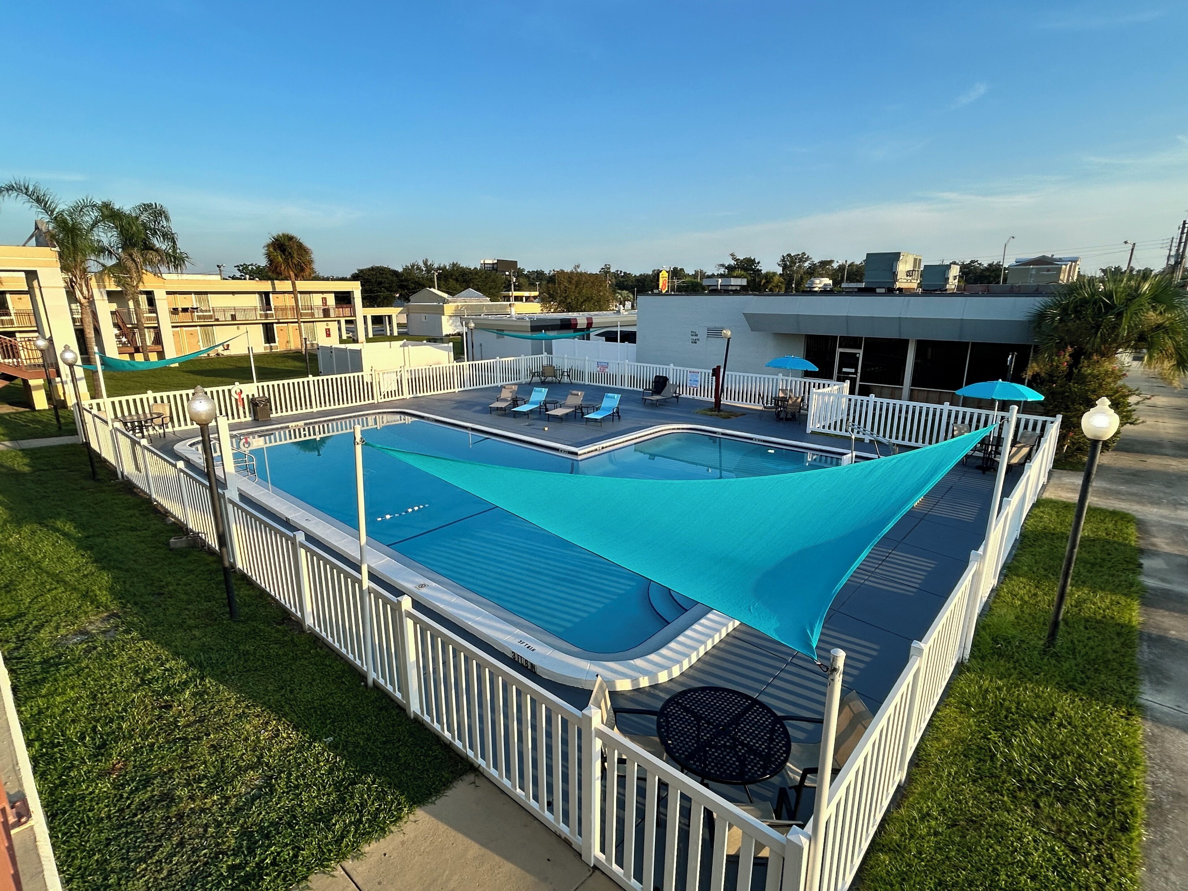 A swimming pool with a white deck and a blue shade sail, surrounded by a white fence.
