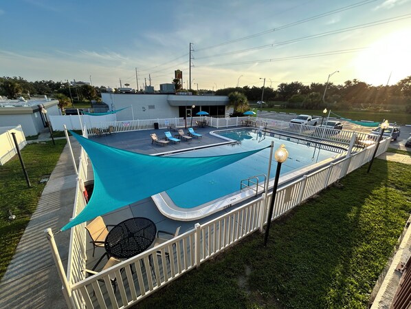 Zona de piscina con una sombrilla, sillas de descanso y una valla blanca.