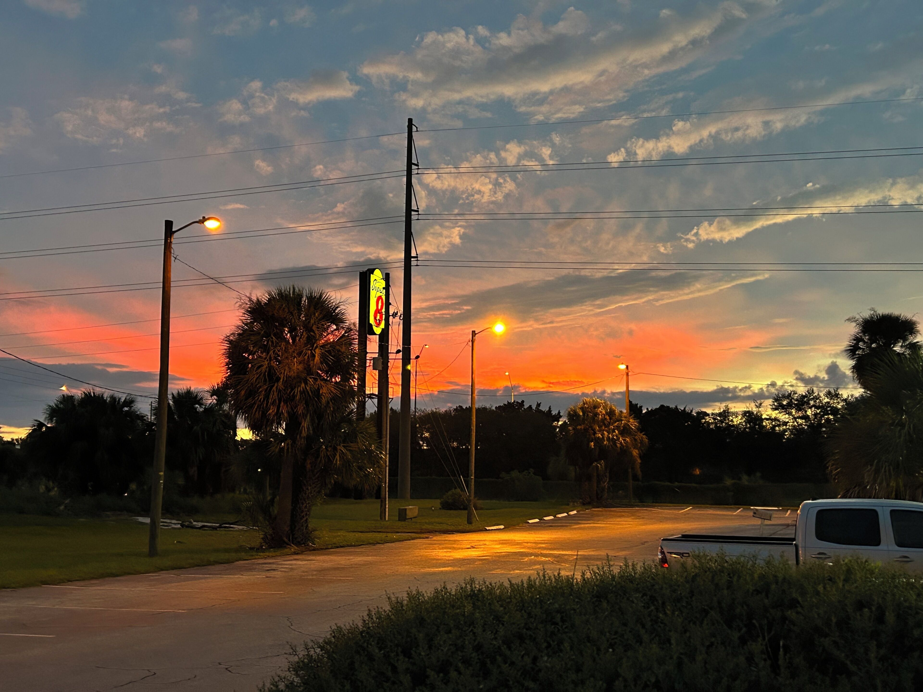 A street at sunset with a street sign, power lines, and a white van.