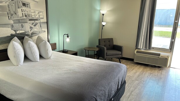 A hotel room with a bed, a chair, a lamp, and a window.