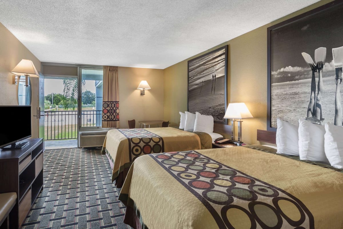 A hotel room with two beds, a TV, a desk, and a balcony with a view of the beach.