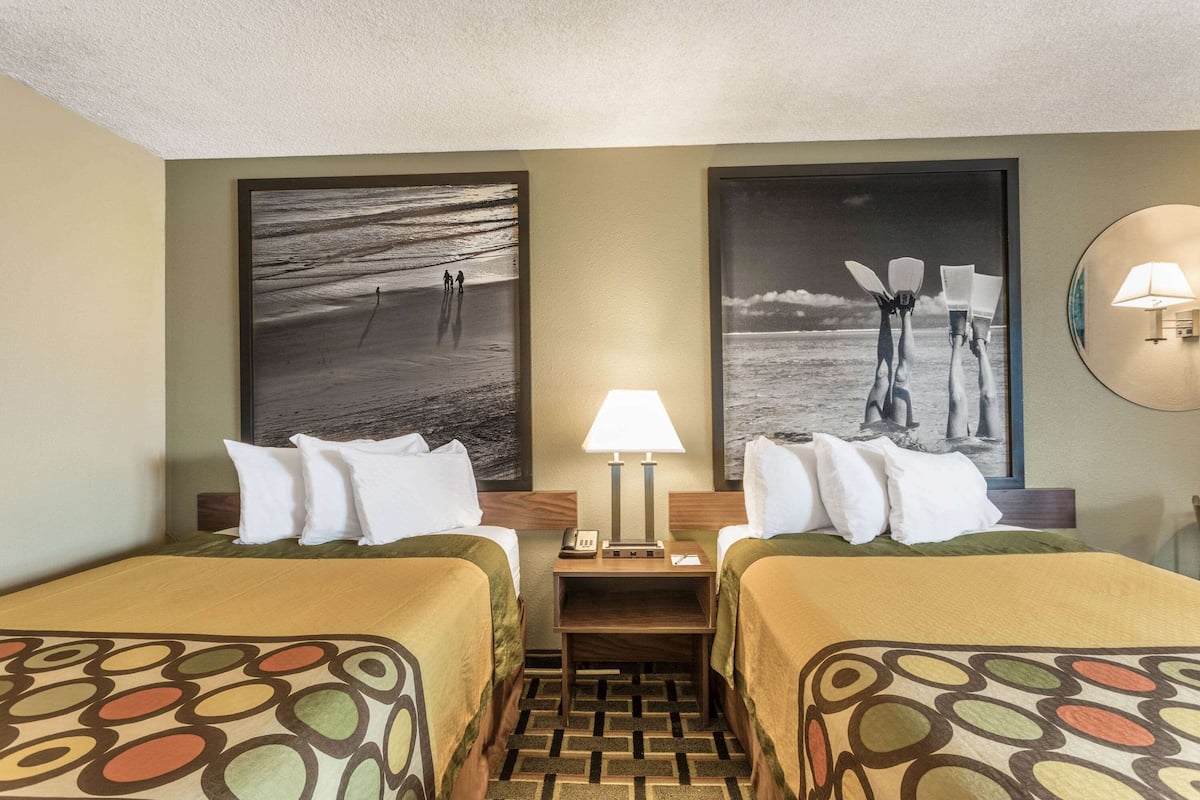 A hotel room with two beds, a nightstand with a lamp, and two large black-and-white photographs on the wall.