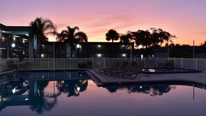 A pool area with lounge chairs and a white fence.